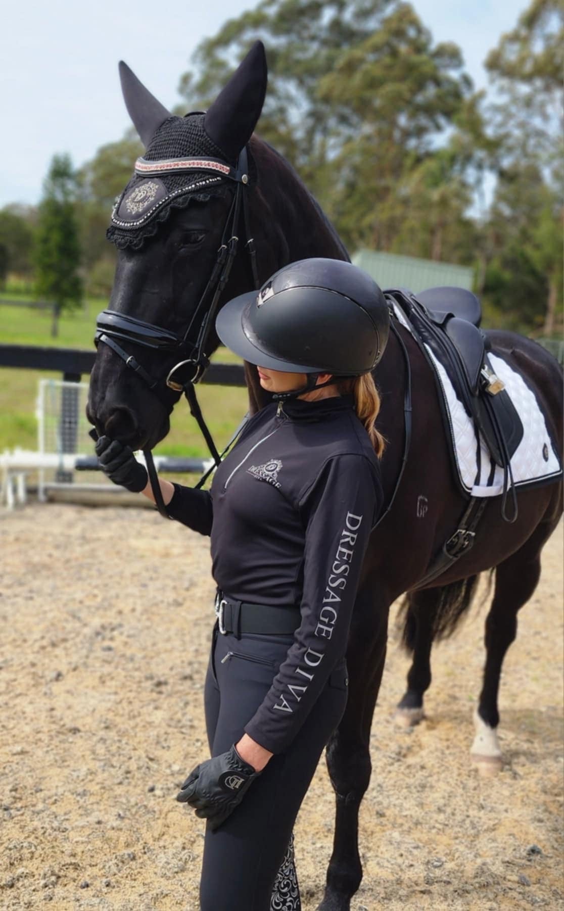 A person wearing a black long sleeve base layer with a grey logo and mesh equestrian shirt standing next to a horse.